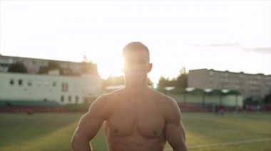 Ağır çekim. Güneşli bir yaz gününde çıplak gövdeli genç bir sporcu kameraya doğru hareket ediyor. Portre görünümünü kapat