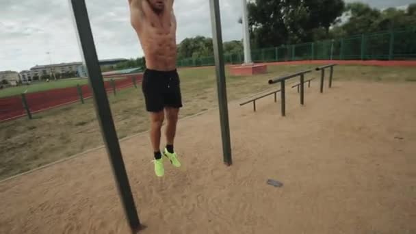 Fit young man doing hanging leg raises exercise on horizontal bar in the street gym — Stock Footage Fit young man doing hanging leg raises exercise on horizontal bar in the street gym Stock Footage
