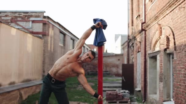 Musclé seins nus jeune gars faire de la calisthénique sur une barre rouge verticale à l'extérieur — Video