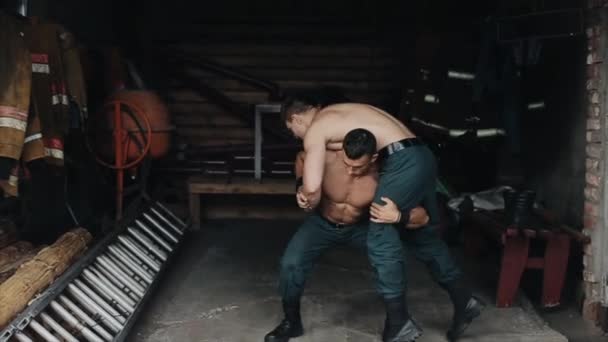 Yakışıklı genç bir adam başka bir ağır adamı omuzlarında tutarak çömeliyor. Kapalı alanda eğitim — Stok video