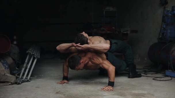 Knappe jonge shirtloze man die push-ups doet met een zware man op zijn rug. Oefenen binnen — Stockvideo