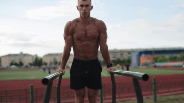 Närbild av en tröjlös muskulös idrottare gör kroppsvikt push-up träna på idrottsplatsen. suddig bild av människor som spelar fotboll på bakgrunden — Stockvideo