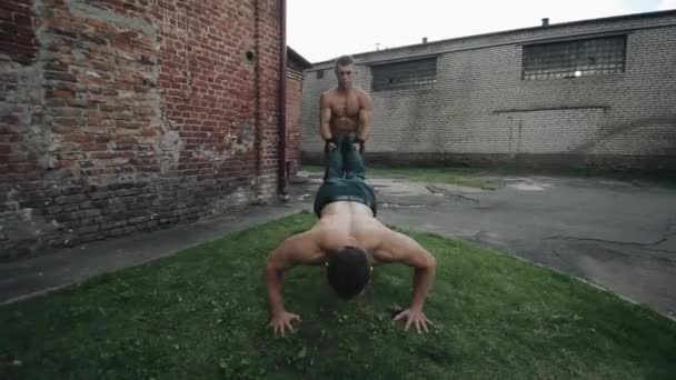 Twee knappe jongemannen lopen kruiwagen en kruiwagen push-ups met klappen buiten — Stockvideo