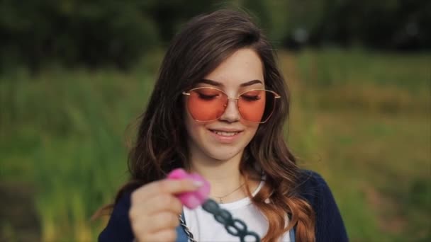 Beautiful young woman in sunglasses blowing soap bubbles outdoors and spinning around. Close view. Slow motion — Stock Video