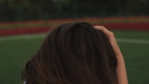 Portrét krásné brunetky žena inblue Sundress sedí na trávníku v blízkosti fotbalového cíle na stadionu. sluneční svit. Dívka s dokonalou postavou a ve skvělé formě. hezká dívka v oranžové — Stock video