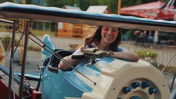 Hermosa joven sonriente en gafas de sol montando un carrusel de niños. Vista cercana. Movimiento lento . — Vídeos de Stock