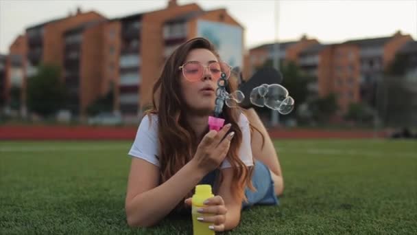 Mulher bonita em óculos de sol soprando bolhas de sabão ao ar livre e girando ao redor. Vista próxima. Movimento lento — Vídeo de Stock