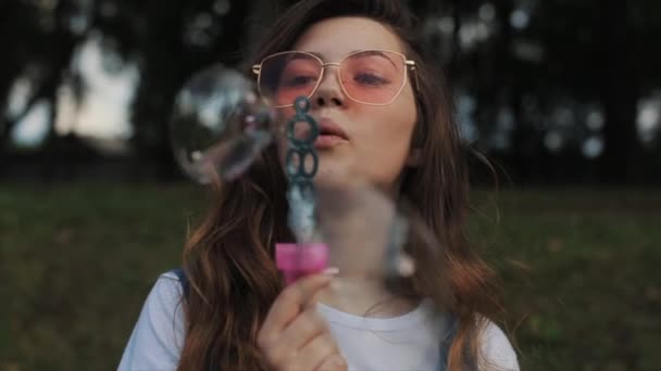 Beautiful young woman in sunglasses blowing soap bubbles outdoors and spinning around. Close view. Slow motion — Stock Video