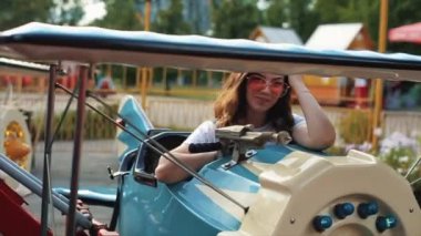 Güneş gözlüklü güzel bir genç kız atlıkarıncaya biniyor. Yakın görüş. Ağır çekim. Güzel kız atlıkarıncaya biniyor.