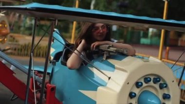 Güneş gözlüklü güzel bir genç kız atlıkarıncaya biniyor. Yakın görüş. Ağır çekim. Güzel kız atlıkarıncaya biniyor.