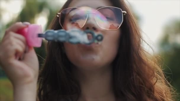 Hermosa mujer joven en gafas de sol soplando burbujas de jabón al aire libre y girando alrededor. Vista cercana. Movimiento lento — Vídeos de Stock