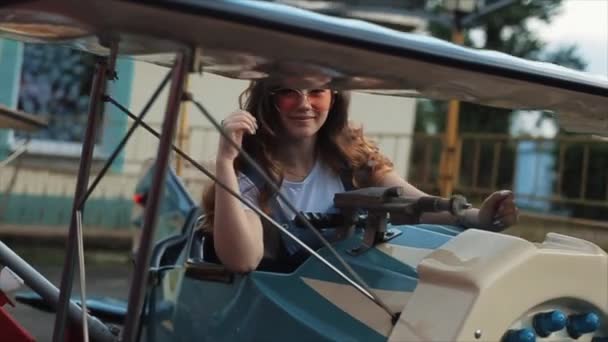 Piękna uśmiechnięta młoda dziewczyna w okularach słonecznych jadąca na karuzeli dla dzieci. Z bliska. Zwolniony ruch — Wideo stockowe