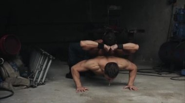 Sırtüstü uzanmış ağır bir adamla şınav çeken yakışıklı genç bir adam. İçerde egzersiz yapmak.