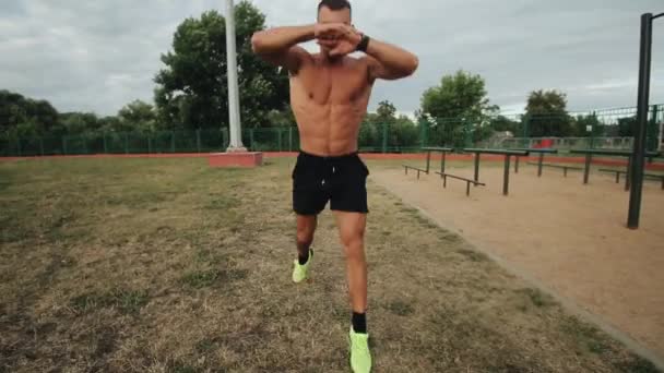 Симпатичный спортсмен делает упражнения по прыжкам с парашютом во время тренировок на стадионе на открытом воздухе — стоковое видео