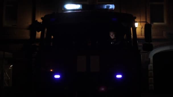 Voor een brandweerwagen met knipperende noodverlichting en sirenes 's nachts. Brandweerman voorin. — Stockvideo