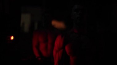 İki kaslı itfaiyeci, geceleri yanıp sönen itfaiye arabasının acil durum ışıkları ışığında biceps egzersizi yapıyor. Yakın görünüm