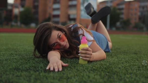 Belle jeune femme en lunettes de soleil soufflant des bulles de savon à l'extérieur et tournant autour. Vue rapprochée. Mouvement lent — Video