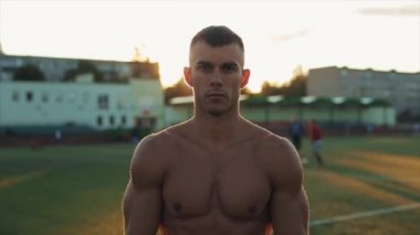 Ağır çekim. Güneşli bir yaz gününde çıplak gövdeli genç bir sporcu kameraya doğru hareket ediyor. Portre görünümünü kapat