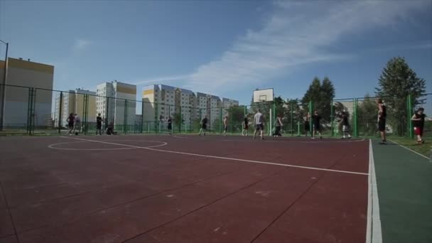 Bobruisk, Belarus - 12 August 2019: Young basketball player making slam dunk during street basketball game. Slow motion. Bright sun in the sky — Stock Video