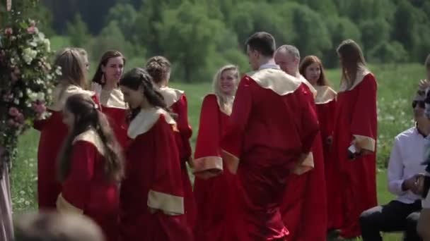 Мінськ, Білорусь - 24 серпня 2019 року: чоловічий і жіночий хор у червоному одязі співають з диригентом перед аудиторією влітку. — стокове відео