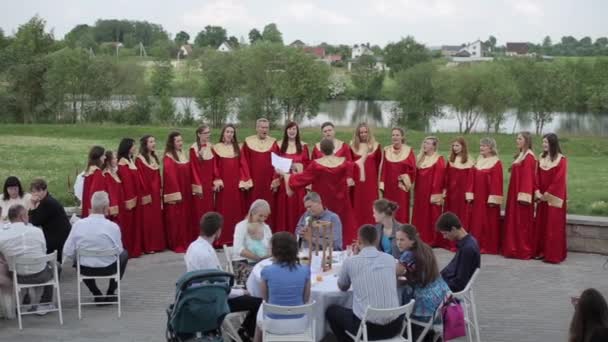 Minsk, Bielorrusia - 24 de agosto de 2019: Feliz hombre y mujer con túnicas rojas cantando con un director en un coro gospel al aire libre — Vídeos de Stock