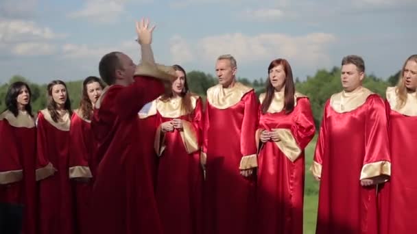 Minszk, Fehéroroszország - 2019. augusztus 24.: Vissza a képre egy karmester, aki nyáron vörös ruhás fiatal férfiak és nők evangéliumi kórusát vezeti szabadtéren — Stock videók
