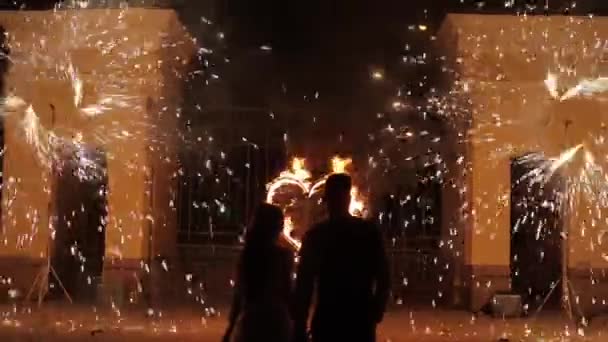 Minsk, Belarus - August 8, 2019: Silhouettes of a wedding couple enjoying fire show. Close rear view. The image becoming defocused — Stok video