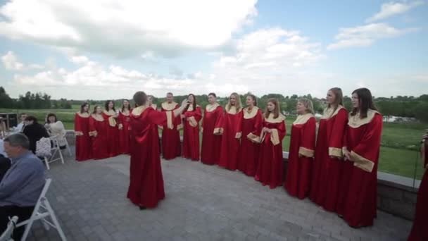 Минск, Беларусь - 24 августа 2019 года: Счастливые мужчины и женщины в красных одеждах поют с дирижером в хоре под открытым небом — стоковое видео