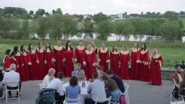 Minsk, Belarus - 24 augustus 2019: Mannelijk en vrouwelijk evangeliekoor in rode gewaden zingen met een dirigent voor het publiek in de zomer buiten — Stockvideo