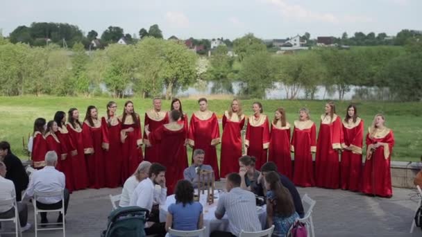 Minsk, Bielorrusia - 24 de agosto de 2019: Coro de gospel masculino y femenino con túnicas rojas cantando con un director de orquesta frente a la audiencia en verano al aire libre — Vídeos de Stock