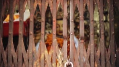 A close-up of a big Buddha statue in a temple in Nepal, Kathmandu through rusty grating. Bokeh blur