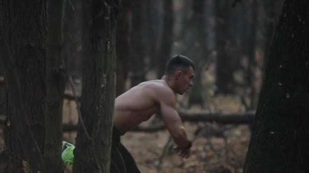 Lonely muscular athlete runs in the forest between the trees with naked torso. Cinematic shot. autumn leaves on the ground. — ストック動画