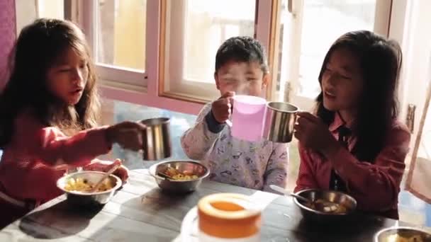Katmandu, Nepal - 14 november 2019: Tre söta nepalesiska barn som äter frukost hemma. De klängde glasögonen, muggar. Ett leende skratt. — Stockvideo