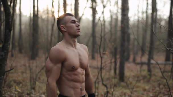 Hombre atlético con el torso desnudo se para en el bosque de otoño hace ejercicios de respiración. hojas de otoño caen de los árboles. Movimiento lento . — Vídeos de Stock