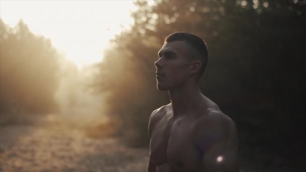 Muskulöser, gutaussehender Mann mit nacktem Oberkörper steht im Wald und atmet tief gegen Sonnenaufgang, Sonnenuntergang, Sonnenaufgang. Zeitlupe. Beschwichtigung — Stockvideo