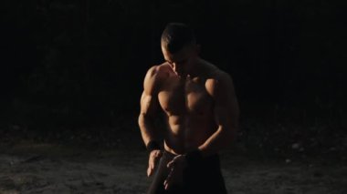 Orman egzersizi. Çıplak gövdesi olan yakışıklı kaslı erkek sporcu ağaç kütüğüyle dışarıda egzersiz yapıyor. Fitness ve sağlıklı yaşam tarzı. Gün batımı. Şafak Gün doğumu
