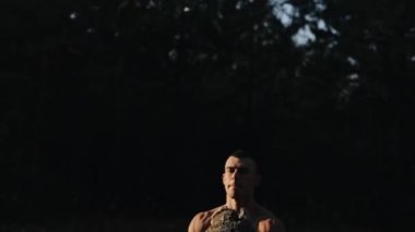 Orman egzersizi. Çıplak gövdesi olan yakışıklı kaslı erkek sporcu ağaç kütüğüyle dışarıda egzersiz yapıyor. Fitness ve sağlıklı yaşam tarzı. Gün batımı. Şafak Gün doğumu