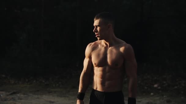 Muskulöser, gutaussehender Mann mit nacktem Oberkörper steht im Wald und atmet tief durch. Morgendämmerung, Sonnenuntergang, Sonnenaufgang. Zeitlupe. — Stockvideo