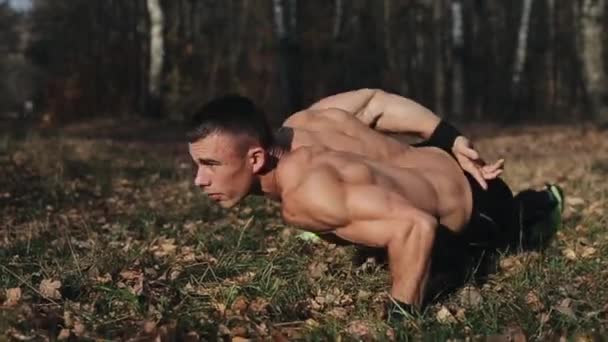 Ung muskulös atletisk man tränar gör armhävningar på ena armen i skogen. Stark kaukasisk kille med naken överkropp — Stockvideo