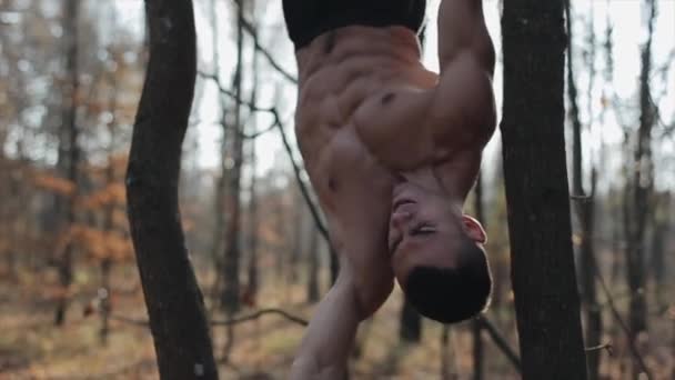 벗은 몸통을 가진 근육질의 남자는 실외의 수평봉을 사용하여 인쇄기로 운동을 한다. — 비디오