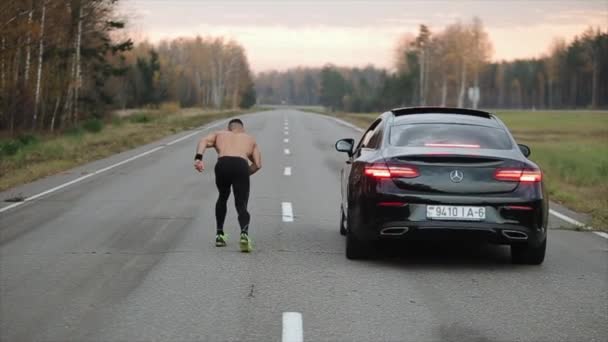 ミンスク、ベラルーシ- 11 11月2019:車に対する男性ランナーのレース。バックビュー。メルセデスEクラスクーペ — ストック動画