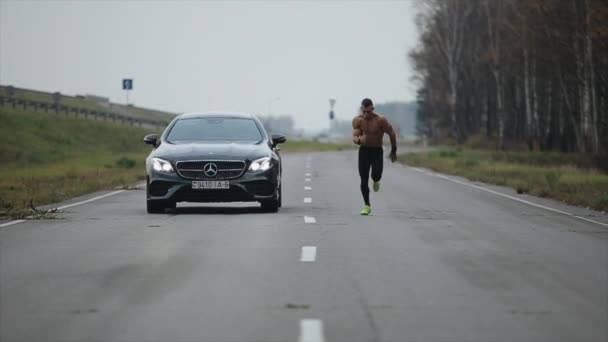 Минск, Беларусь - 11 ноября 2019 года: Мускулистый человек с обнаженным туловищем бьет автомобиль в гонке. Mercedes E-класса Coupe — стоковое видео