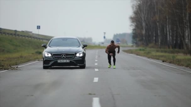 Minsk, Belarús - 11 de noviembre de 2019: Un hombre musculoso con el torso desnudo golpeando a un coche en una carrera. Mercedes E-Class Coupe — Vídeos de Stock