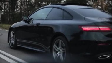 Minsk, Belarus - 11 Kasım 2019: Araba tarlalar ve ormanlar boyunca uzanan kırsal bir yolda ilerliyor. Siyah Mercedes E-Sınıfı Coupe