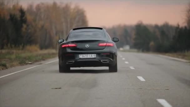 ミンスク、ベラルーシ- 11月2019:車はフィールドや森林を走る田舎道に乗っています。ブラックメルセデスEクラスクーペ — ストック動画