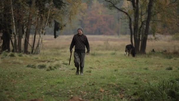 Bobruisk, Vitryssland - 14 oktober 2019: En man går med yxa i händerna längs gräset bland träden — Stockvideo