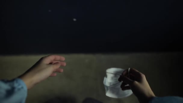 A man putting on, wearing a medical flu mask against coronavirus. POV. Black background. — Stock Video