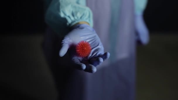 Närbild av en forskare i skyddande medicinska kläder, kostym pekar på kameran en coronavirus Covid-19 modell. Mörk bakgrund. — Stockvideo