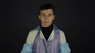 Tıbbi maske takmakta zorlanan beyaz bir adam. Gülüyor, gülümsüyor. Coronavirus. Koyu arkaplan.