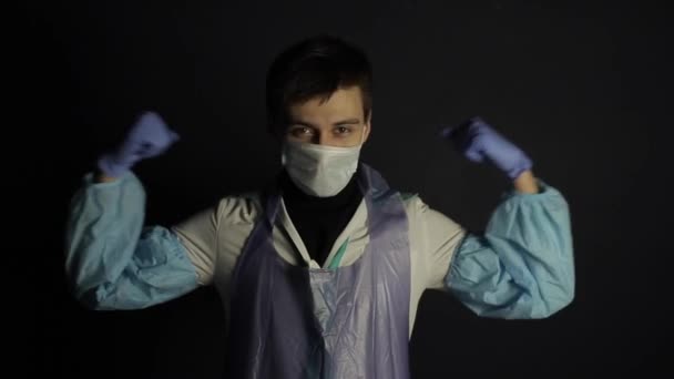 A caucasian man doctor wearing protective medical suit showing his biceps, strength. Black dark background. Supporting. COVID-19 — Stock Video